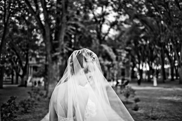 black and white photo - gorgeous photo of a beautiful bride wearing a full length veil with hair in an updo looking down as she stands in a yard full of old oak trees - photo by New Mexico based wedding photographers Twin Lens